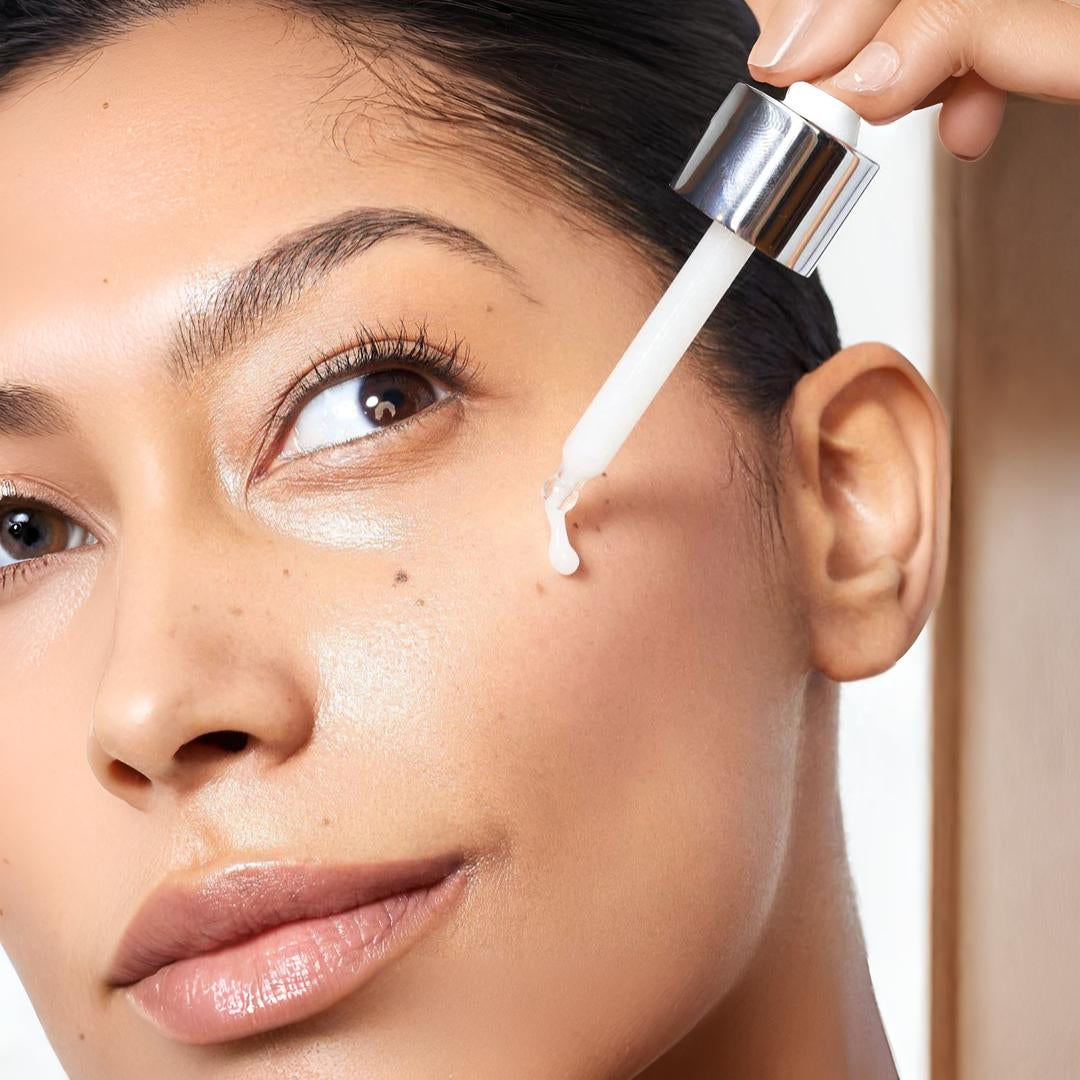 Woman applying Clinical Skin Polypeptide Firming Serum with dropper – model with smooth glowing skin applying firming serum to cheekbone to lift, tighten and firm facial contours