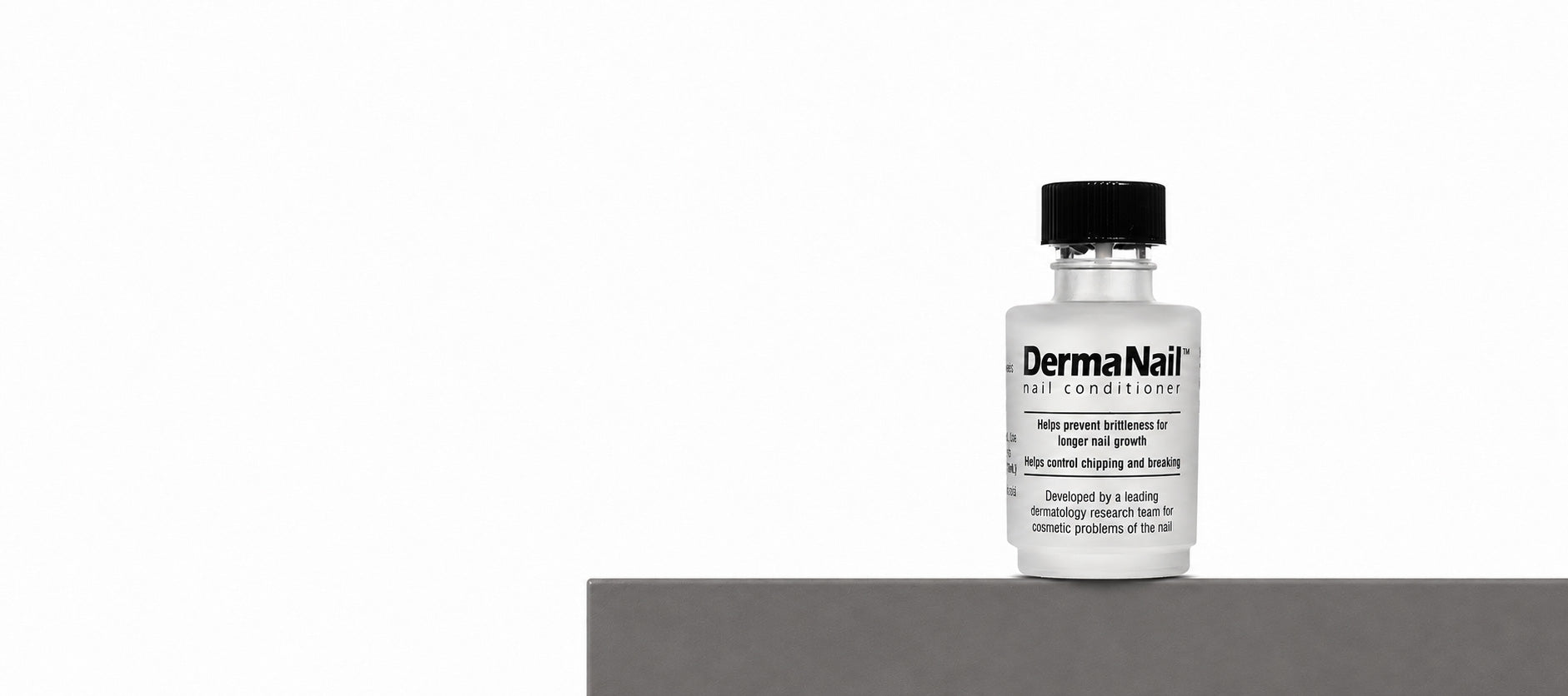 A small clear bottle of DermaNail Soft Enhancer with a black cap, standing on a dark gray platform against a plain white background.