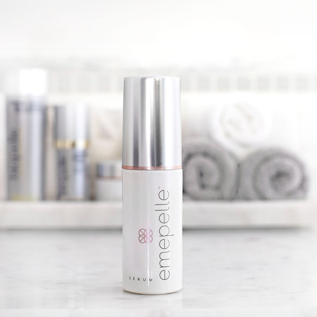 Emepelle Serum white pump bottle on marble counter with skincare products and towels – daily anti-aging serum for menopausal and peri-menopausal skin