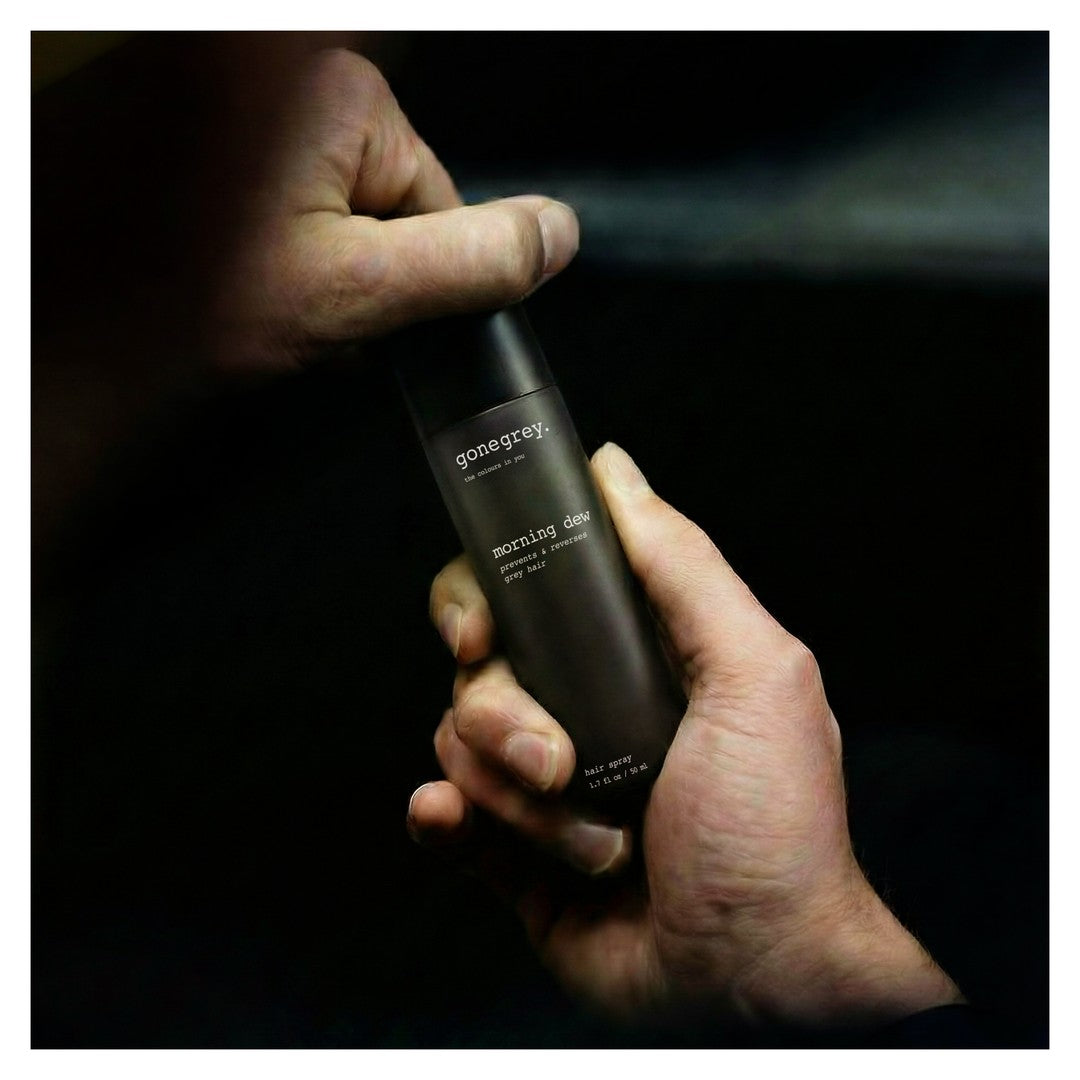 Man holding a bottle of GoneGrey Morning Dew hair spray in a dark, moody lifestyle shot