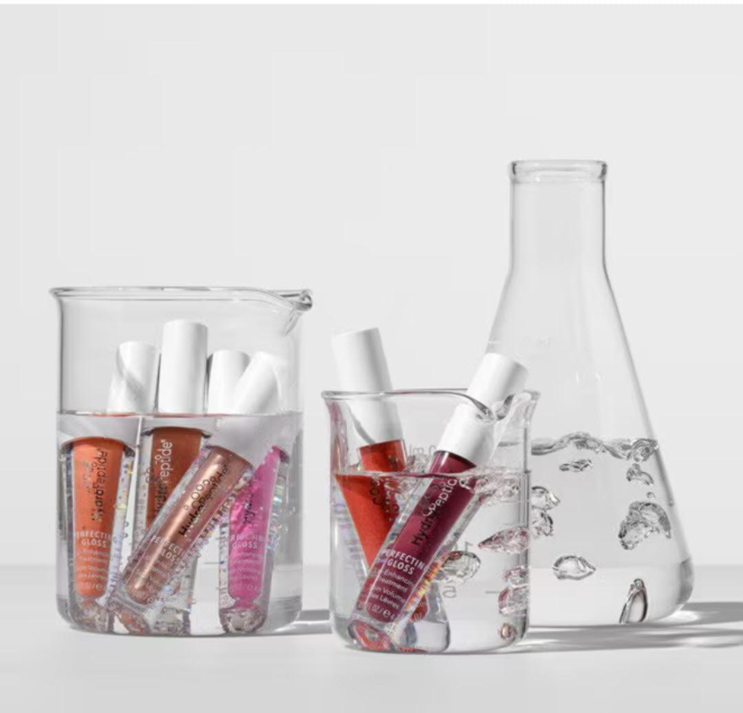 HydroPeptide Perfecting Gloss tubes in Beach Blush, Sunkissed Bronze and Palm Spring Pink displayed in glass beakers