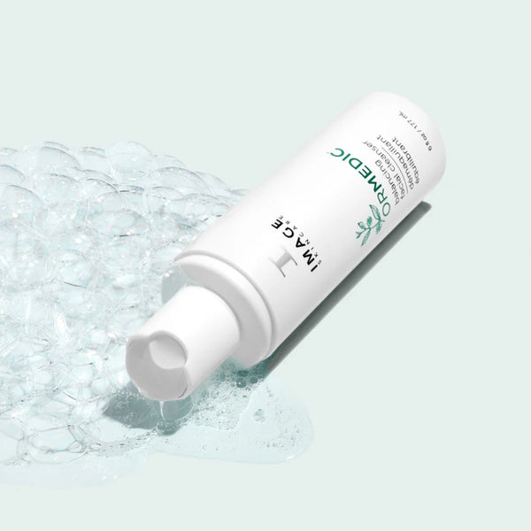 Image Skincare ORMEDIC Balancing Facial Cleanser shown tipped sideways with rich lathering foam bubbles illustrating the gentle pH-balanced cleansing formula