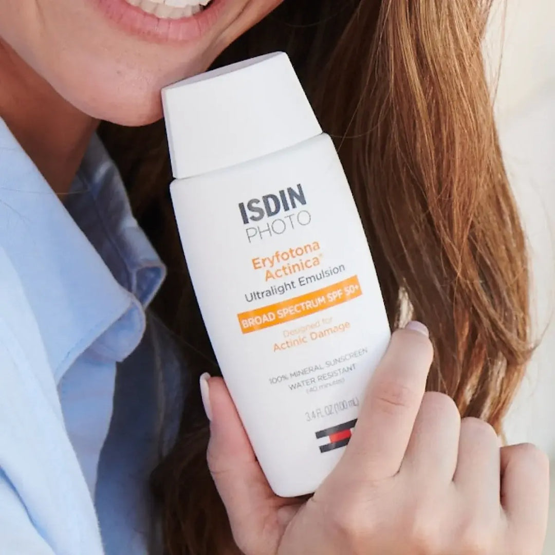 Smiling woman holding ISDIN Eryfotona Actinica sunscreen bottle near her neck