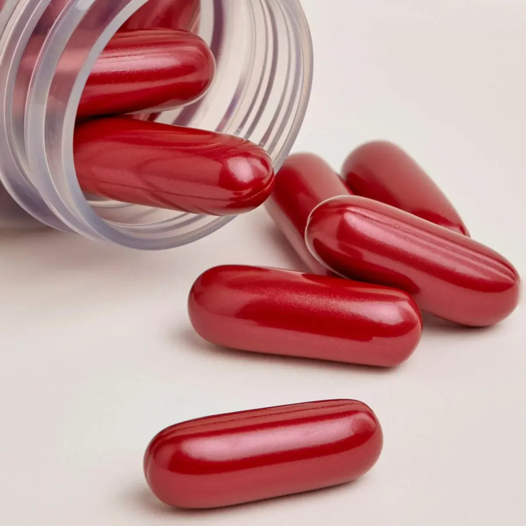 Close up of dark red ISDIN Lambdapil Hair Density For Him capsules spilling out of the bottle