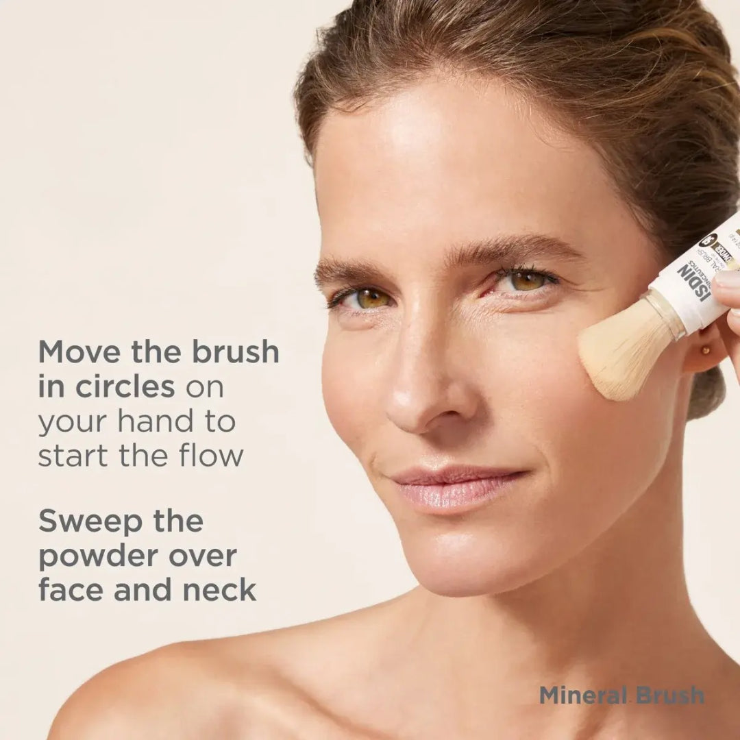 Woman applying ISDIN Mineral Brush to cheek with instructions move the brush in circles on your hand to start the flow then sweep the powder over face and neck