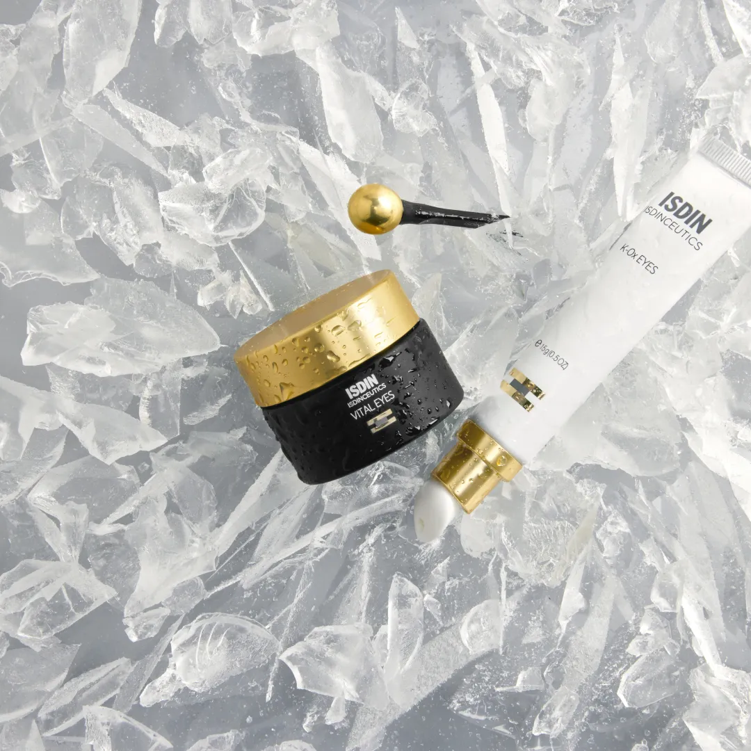 ISDIN Vital Eyes jar with gold ball applicator beside ISDIN K-Ox Eyes tube on shattered ice