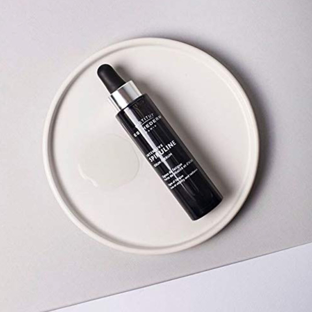 Institut Esthederm Intensive Spiruline Serum dropper bottle resting on a white plate with a drop of serum