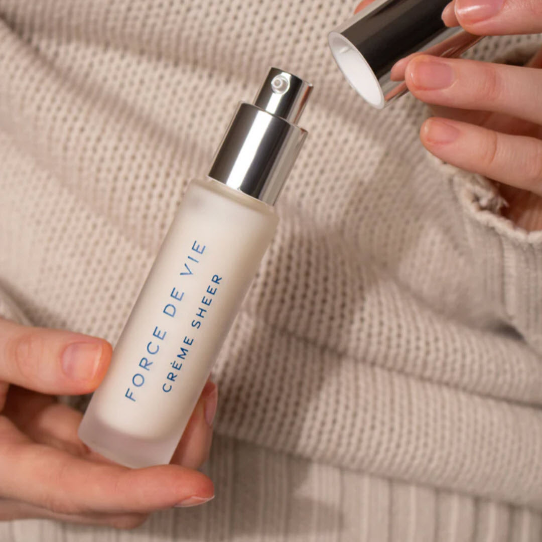 Woman holding a bottle of Luzern Force De Vie Creme Sheer while removing the cap