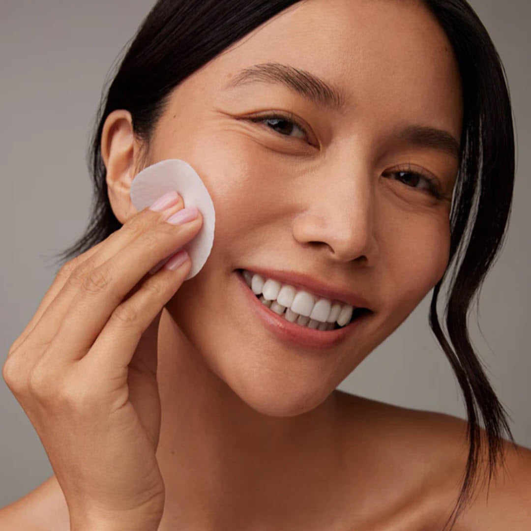 Woman smiling while sweeping a Luzern L'Essentials AHA Exfoliating Pad across her cheek