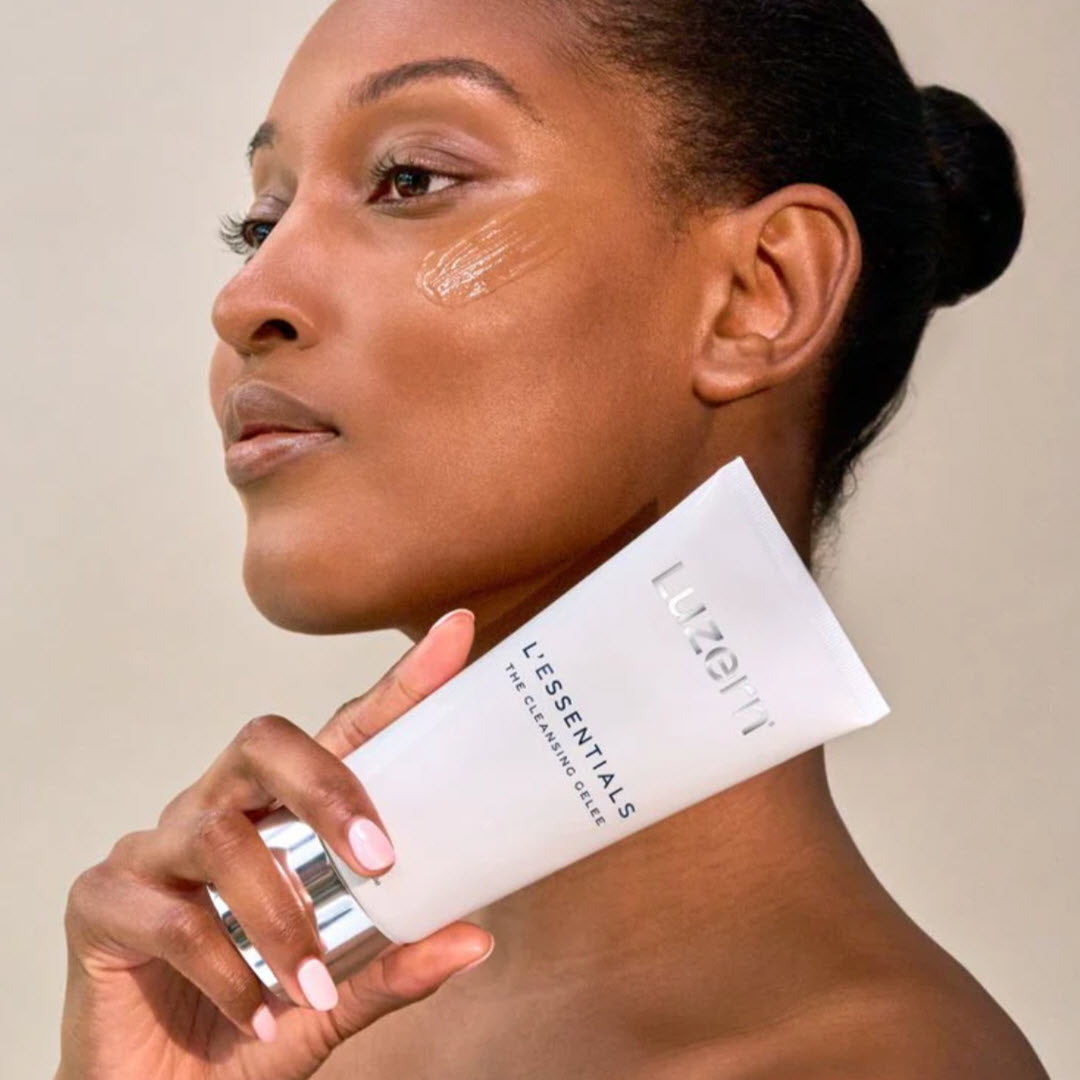 Woman holding a tube of Luzern L'Essentials Pure Cleansing Gelee near her cheek with product applied under her eye