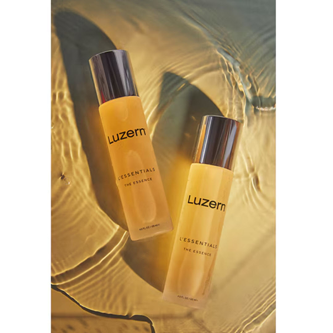 Two bottles of Luzern L'Essentials The Essence Hydration Infusion Essence styled in golden water