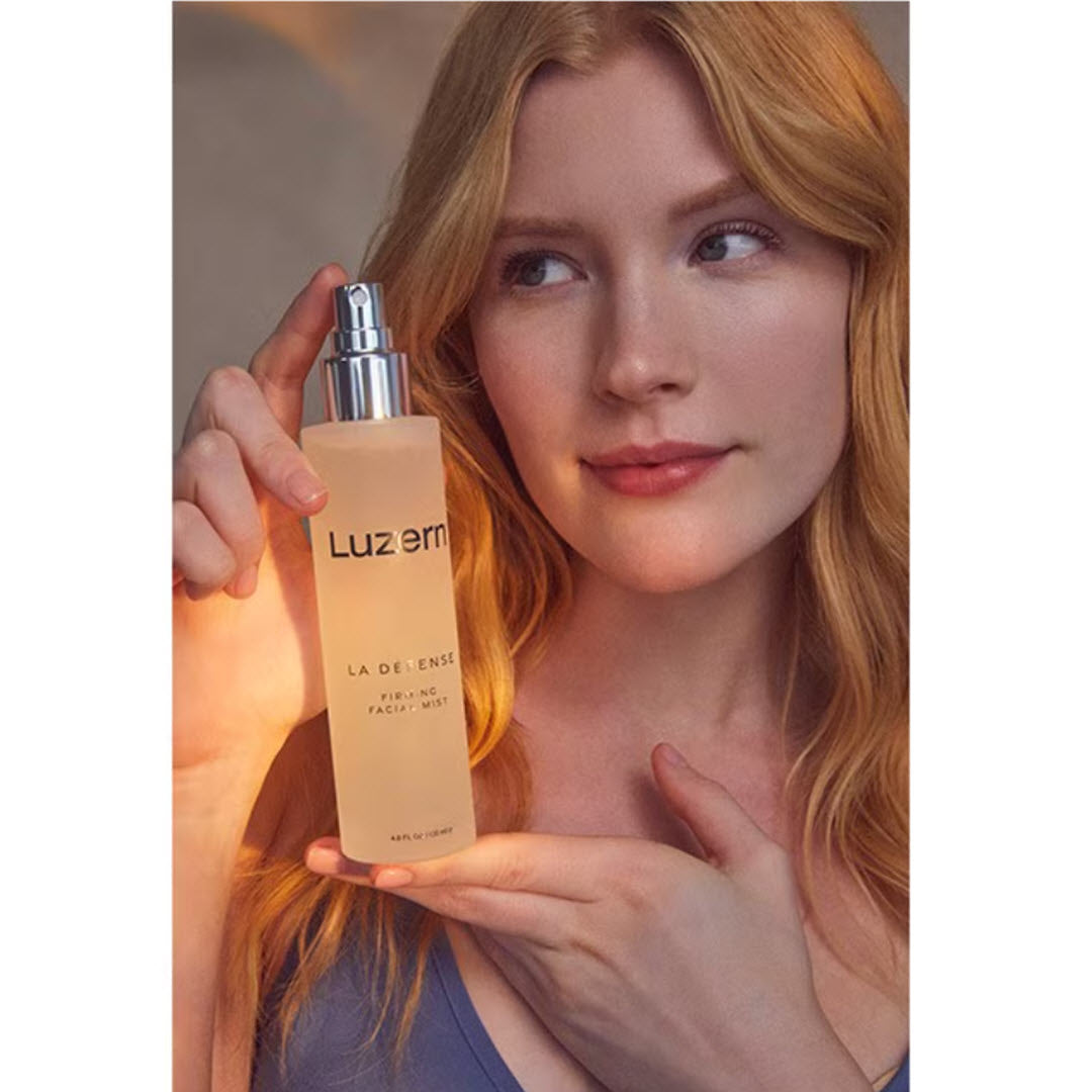 Woman holding a bottle of Luzern La Defense Firming Facial Mist near her face