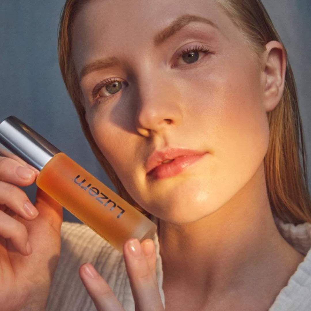 Woman holding a bottle of Luzern Serum Absolut Radiance Brightening Booster Complex next to her face