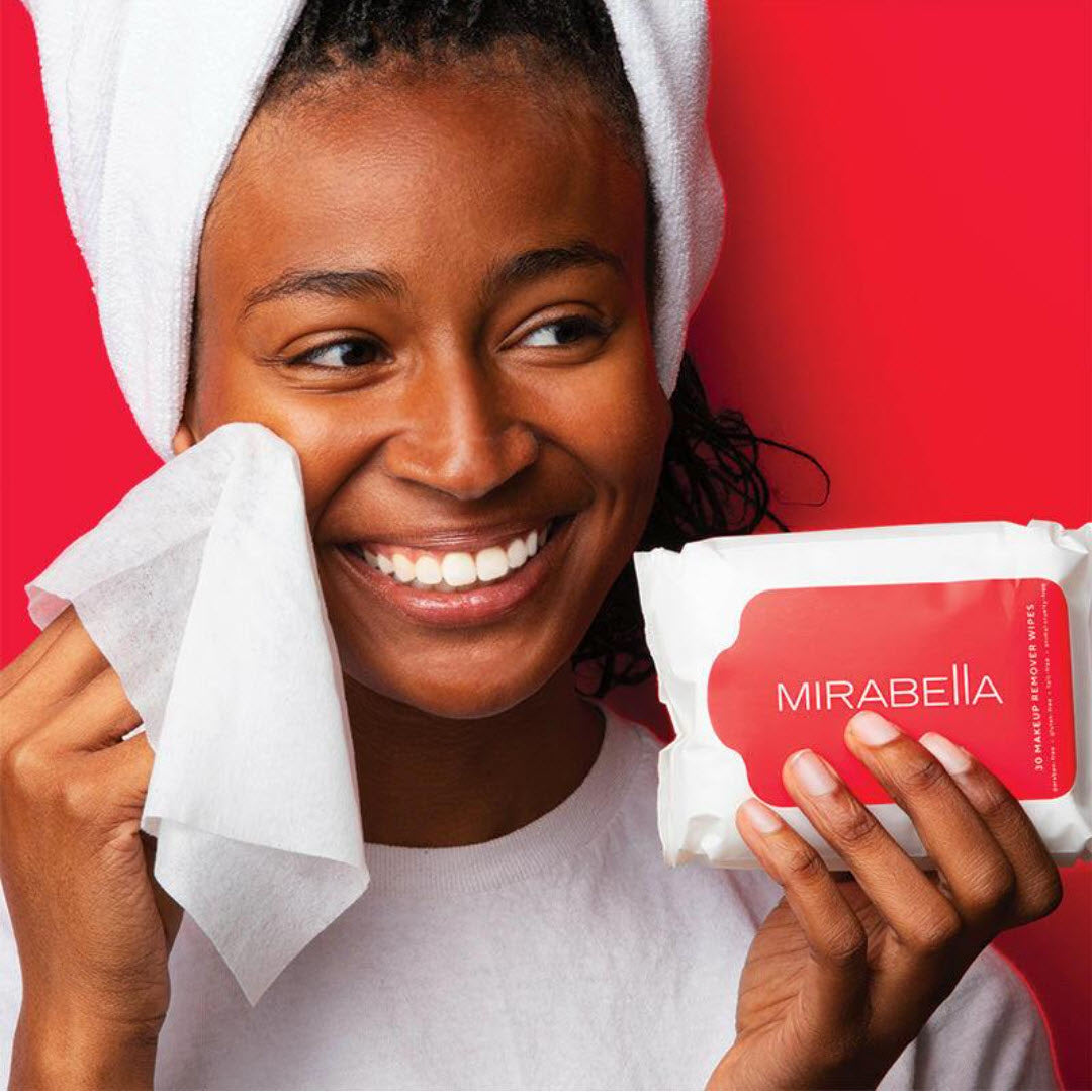 Model wiping face with a Mirabella Makeup Remover Wipe while holding the 30-count pack