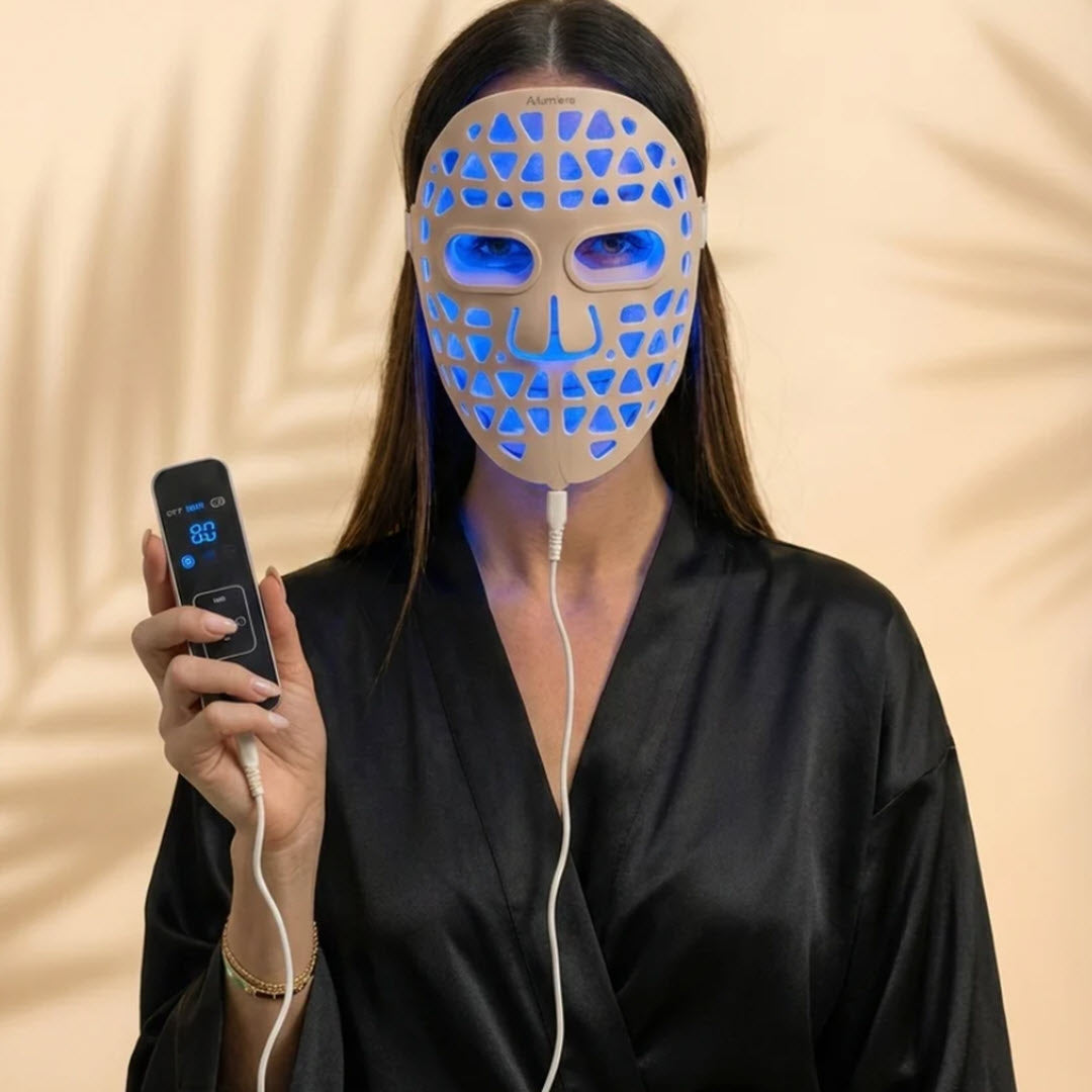Woman wearing the Numiere Feather LED Face Mask with blue light therapy, holding the handheld controller