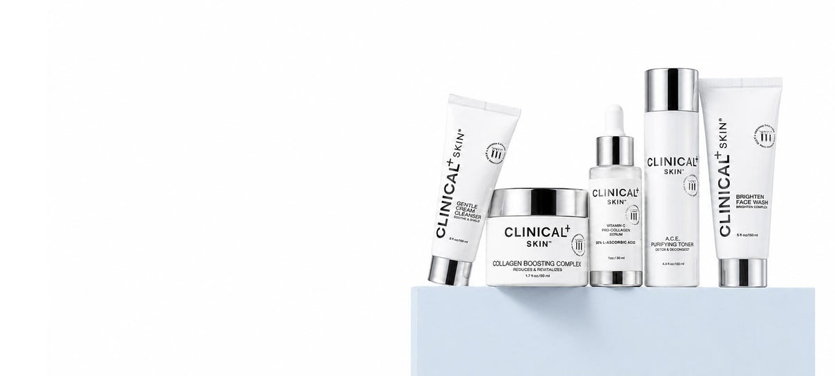 A group of white and silver skincare products from Clinical Skin, including tubes, a jar, and a dropper bottle, arranged on a light blue pedestal against a white background.
