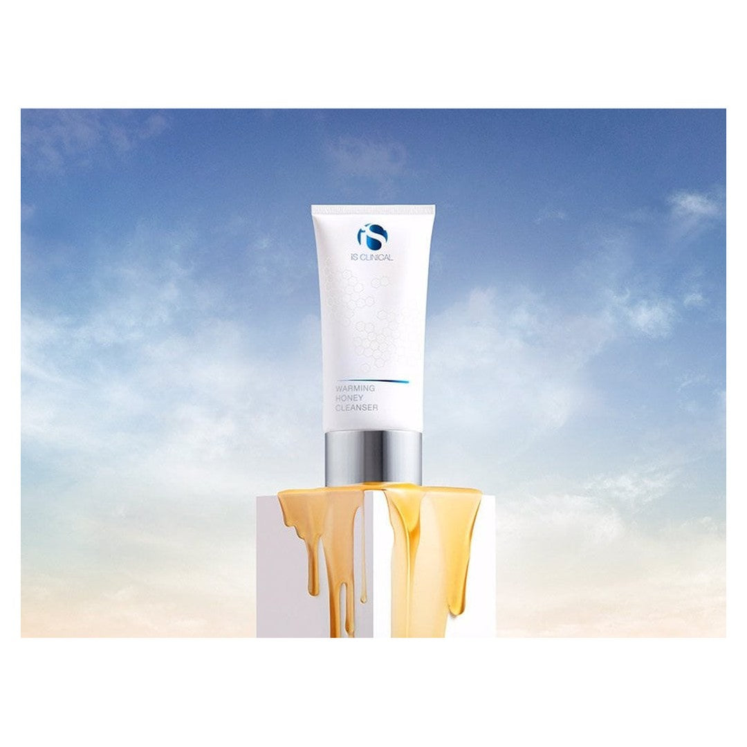 iS Clinical Warming Honey Cleanser tube with golden honey texture dripping down a pedestal against a sky background