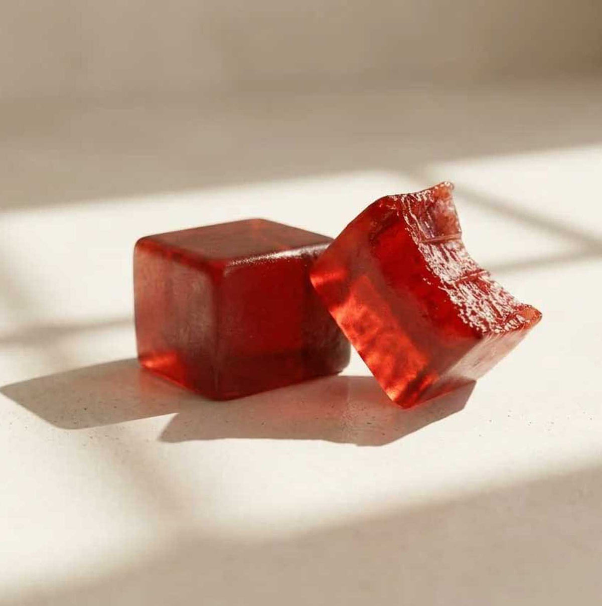 Advanced Dermatology Xtressé Hair Growth Gummies close-up – two translucent red strawberry-flavored sugar-free hair growth gummy cubes on cream background with soft natural light